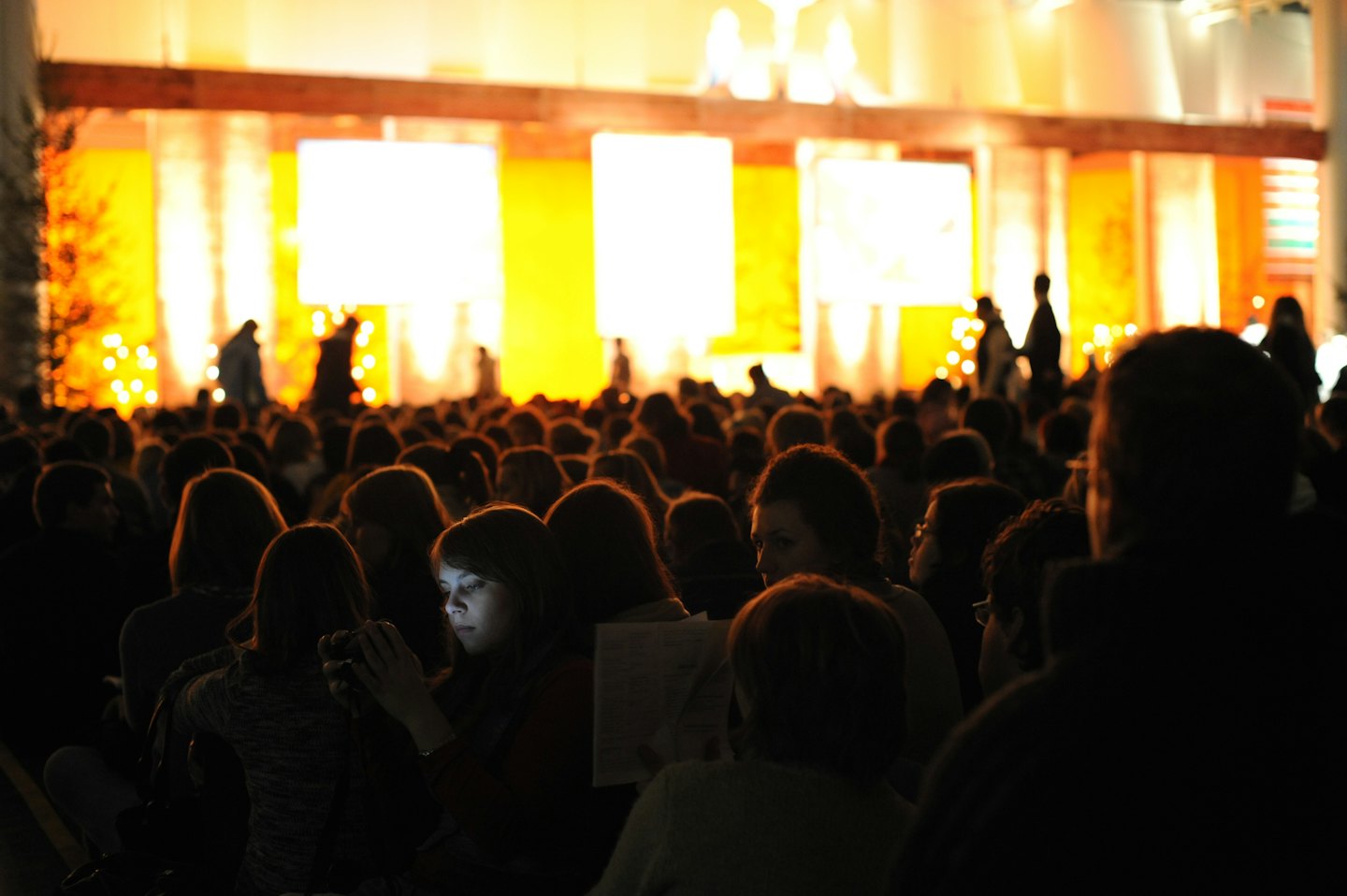 Audience members watch a brightly lit stage in an auditorium.